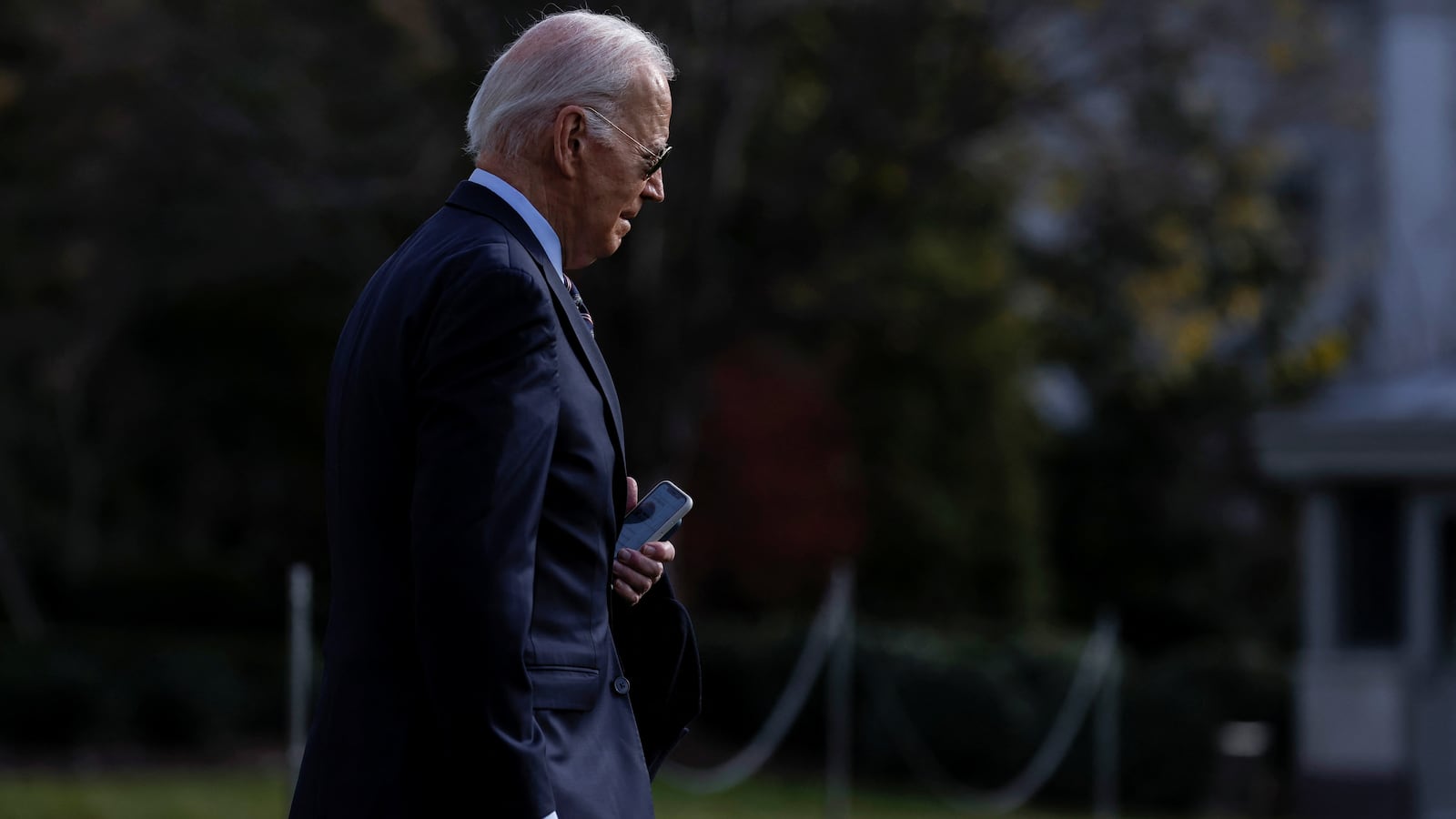 Joe Biden has his head down and phone in hand as he walks out of the White House.