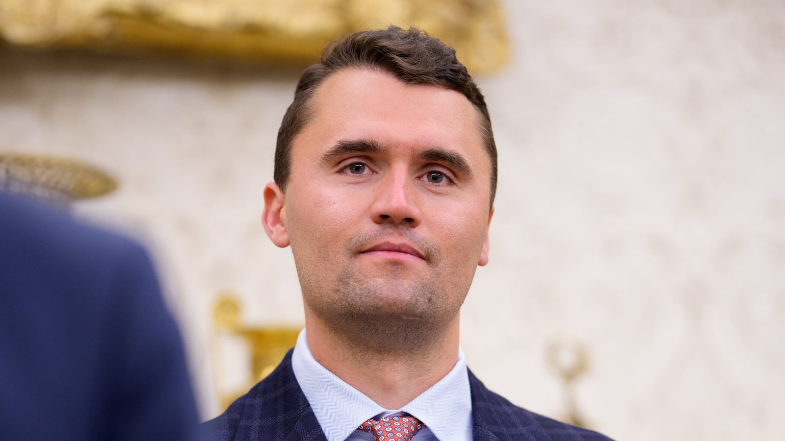 Turning Point USA co-founder Charlie Kirk stands in the back of the room as U.S. President Donald Trump speaks during a swearing in ceremony