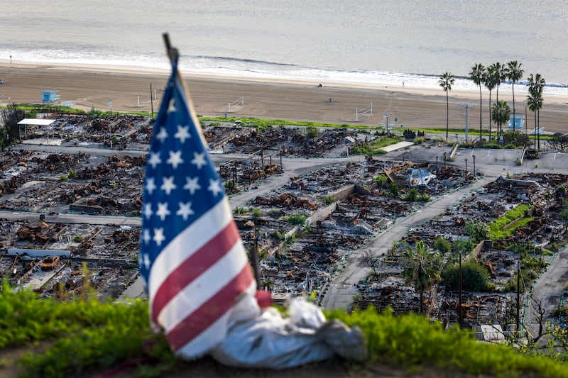 Pacific Palisades, CA - January 06: An American flag and sand bag stands on a cliff overlooking the remains of the Pacific Palisades Bowl Mobile Estates, which was destroyed in the 2025 Palisades fire, on the one year anniversary in Pacific Palisades Tuesday, Jan. 6, 2026.  (Allen J. Schaben / Los Angeles Times via Getty Images)