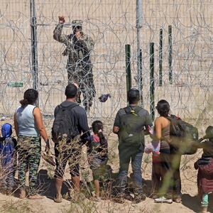 Migrants seeking asylum in the U.S. speak with a Texas National Guard agent through a barbed-wire fence.