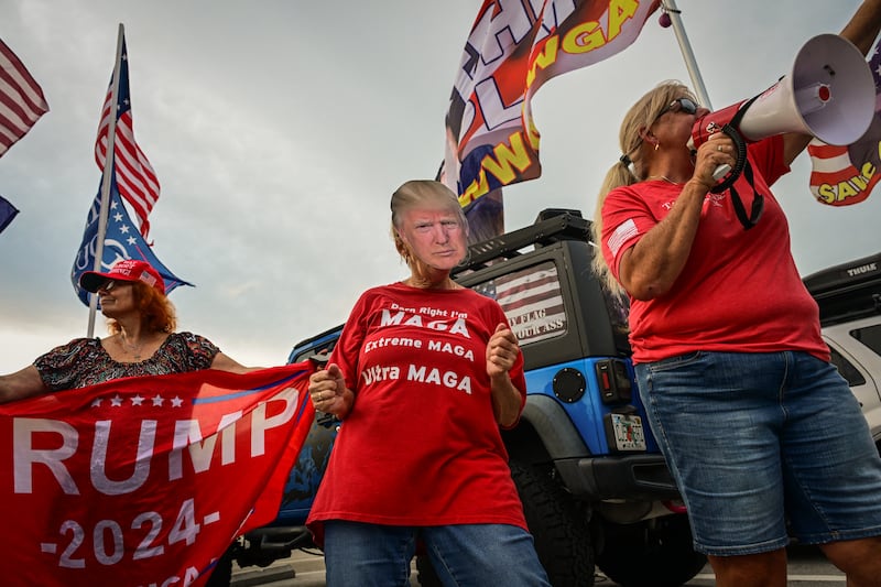 A Trump supporter wears a Trump mask as protesters (out of frame) gather near the Mar-a-Lago residence of US President Donald Trump during a rally as part of the 'Good Trouble Lives On' national day of action against the Trump administration in West Palm Beach, Florida, on July 17, 2025.