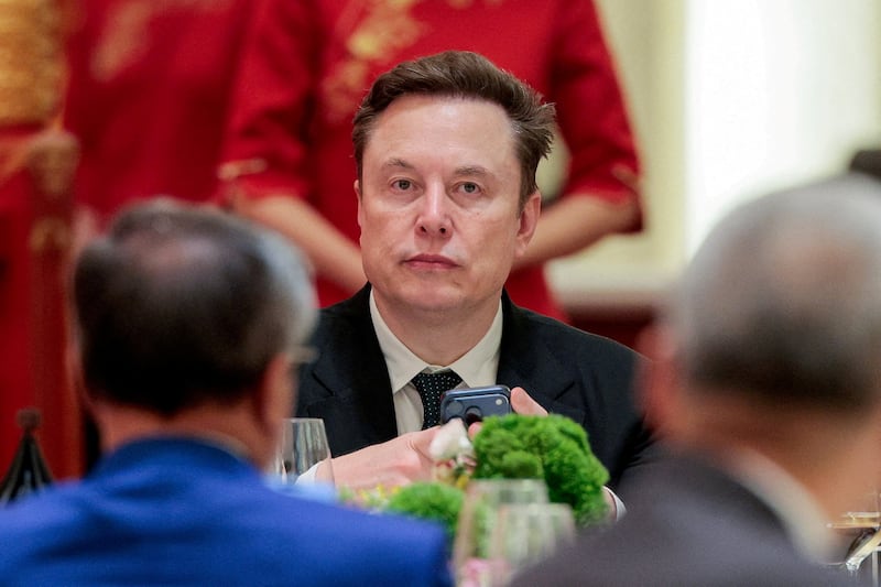 Tesla CEO Elon Musk holds a mobile phone as he arrives to attend a state banquet with U.S. President Donald Trump and Chinese President Xi Jinping at the Great Hall of the People in Beijing, China, May 14, 2026.