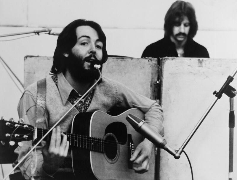 Paul McCartney plays guitar and sings with Ringo Starr in the background of a still from ‘Let it Be’