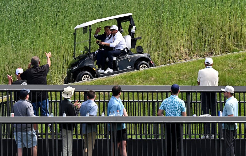 President Donald Trump waves at LIV Golf spectators as he rides as a passenger in a golf cart on May 9.
