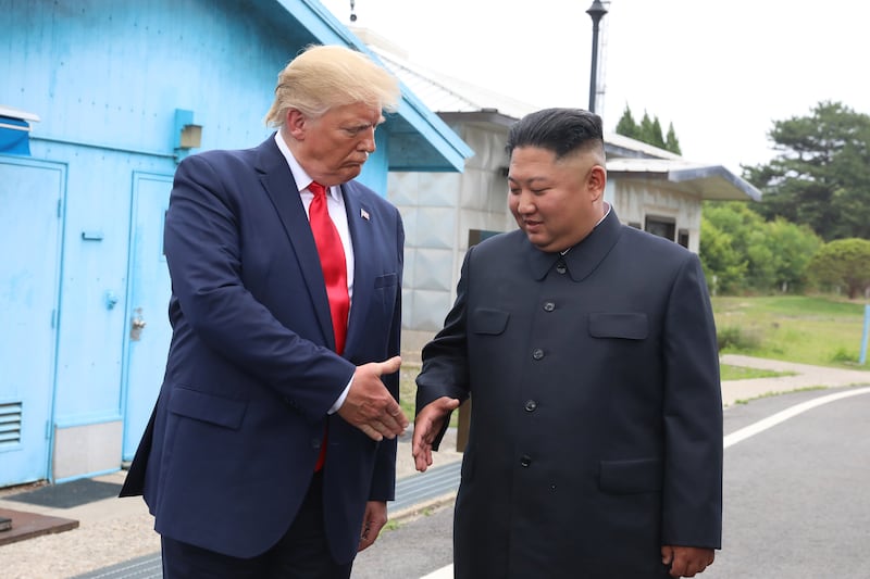 Donald Trump and Kim Jong-Un shake hands.