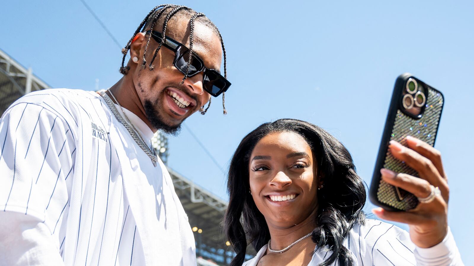 Jonathan Owens smiles alongside Simone Biles on the field at a baseball game.