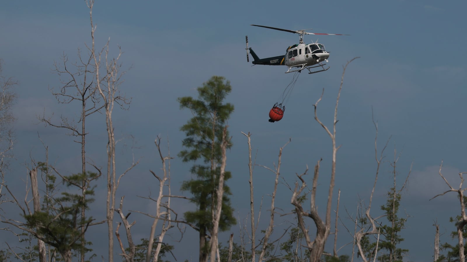 NAPLES, FLORIDA - APRIL 14: A Florida Forest Service helicopter flies to get another load of water to put on a wildfire on April 14, 2026, in Naples, Florida. More than 1,500 acres have burned with the fire at 40% containment, according to the Florida Forestry Service. The historic drought has triggered evacuations in the area. (Photo by Joe Raedle/Getty Images)