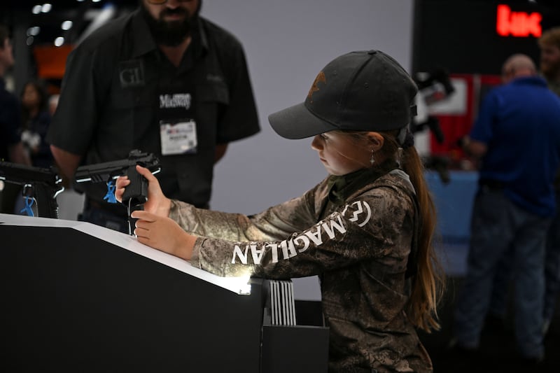 A girl holds a handgun as her father looks on during the National Rifle Association's (NRA) annual meetings and exhibits in Houston, Texas, U.S. April 19, 2026.