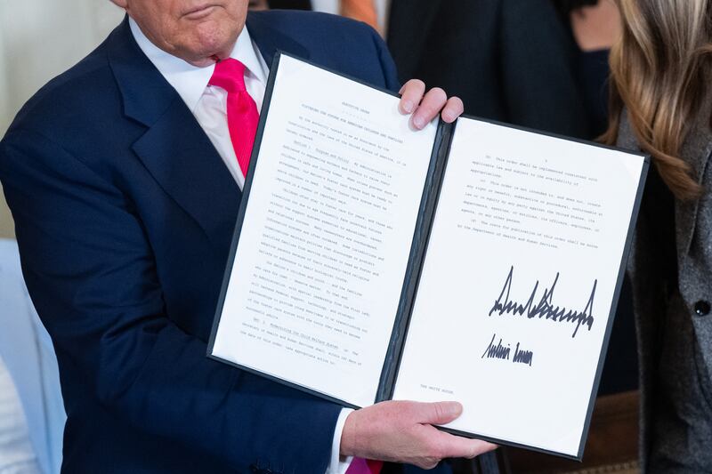 President Donald Trump holds up the signed executive order in the East Room of the White House on November 13, 2025.