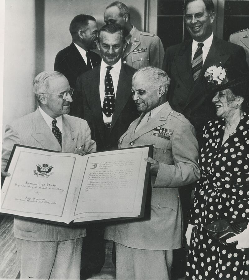 An archival photo of President Truman presenting Ollie with a scroll surrounded by other politicians.