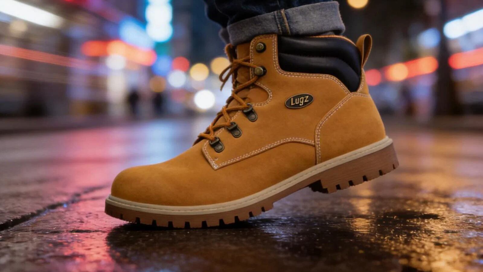 A Lugz lace-up boot in tan/wheat stepping on a wet city street at night, with blurred neon lights in the background.