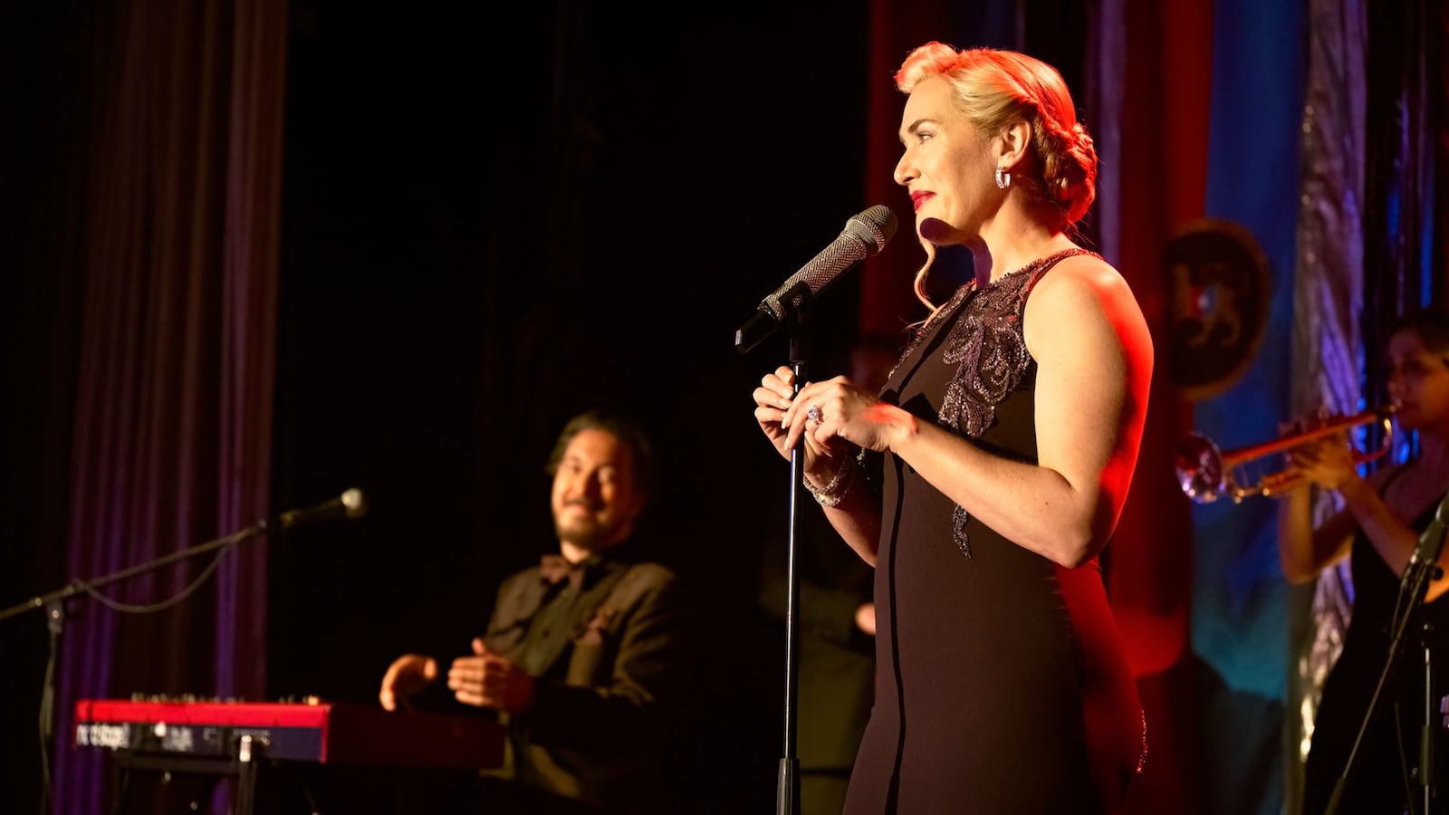Kate Winslet stands at a microphone in a still from ‘The Regime’