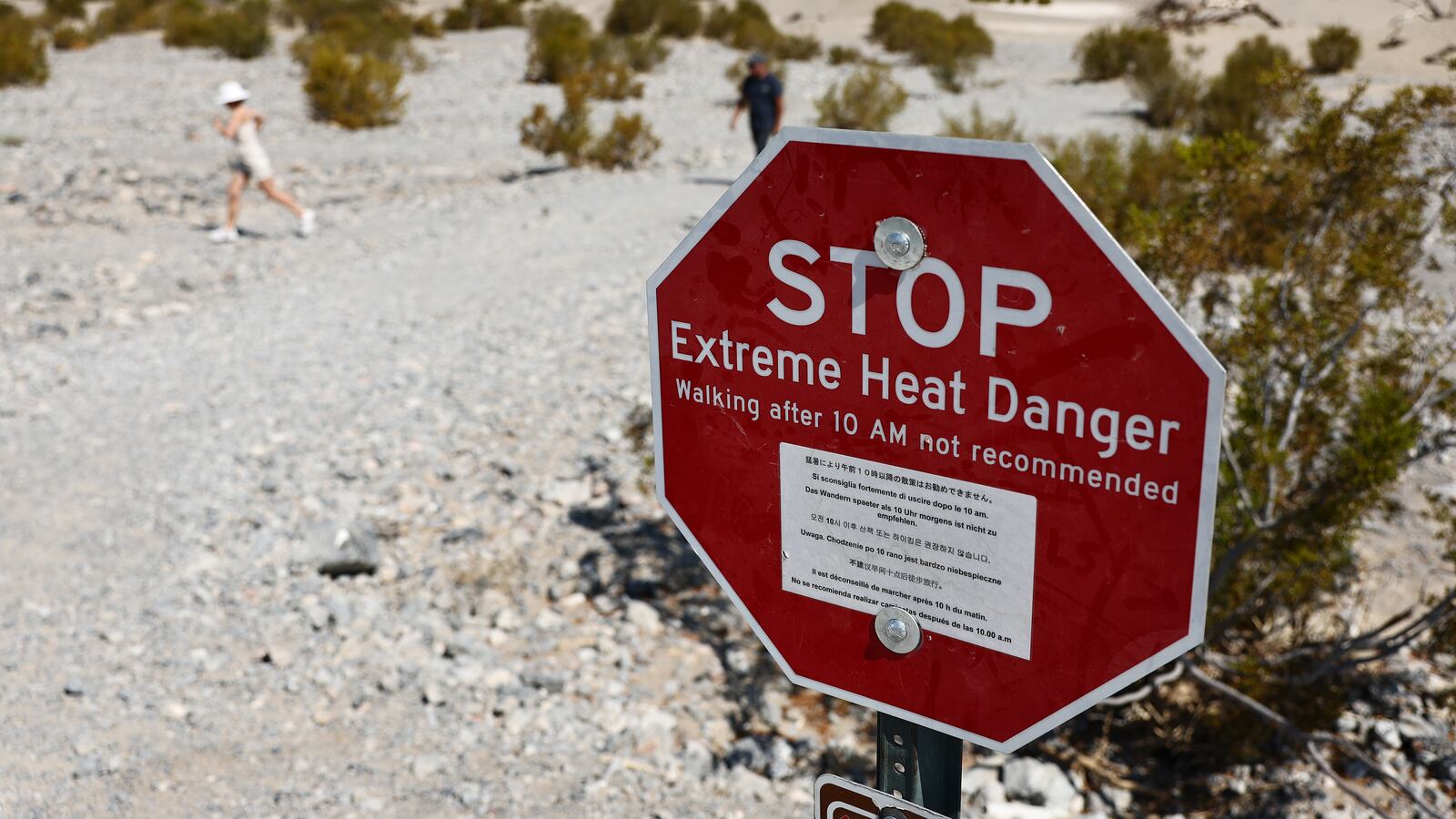 Visitors walk near a 'Stop Extreme Heat Danger' sign at Mesquite Flat Sand Dunes in Death Valley National Park, California.