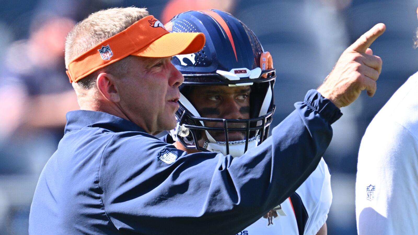 Russell Wilson, in uniform, speaks to Broncos Head Coach Sean Payton on the sideline.
