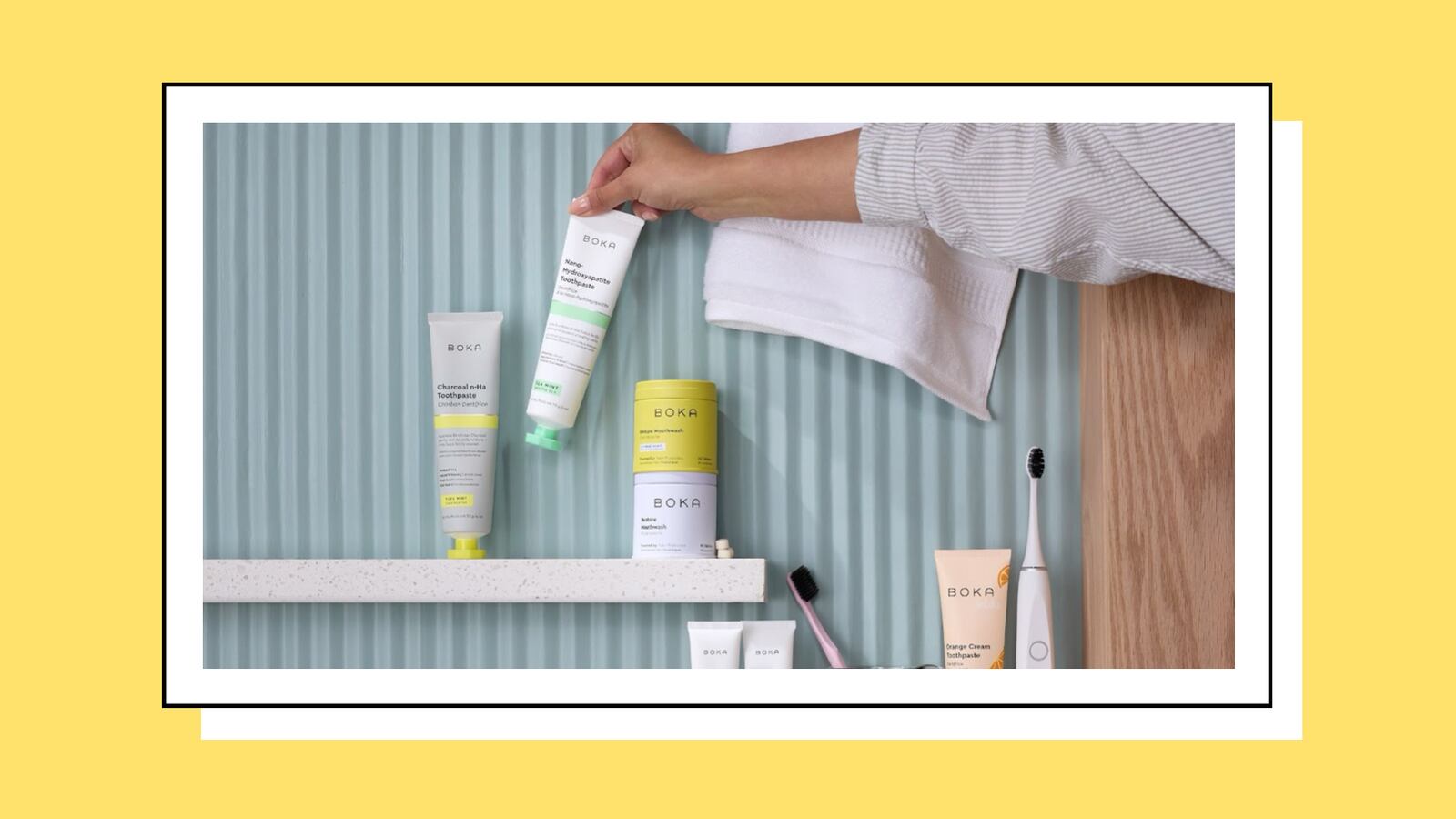 Woman placing a tube of toothpaste on a shelf next to a collection of creams, toothbrushes, and other bathroom amenities.