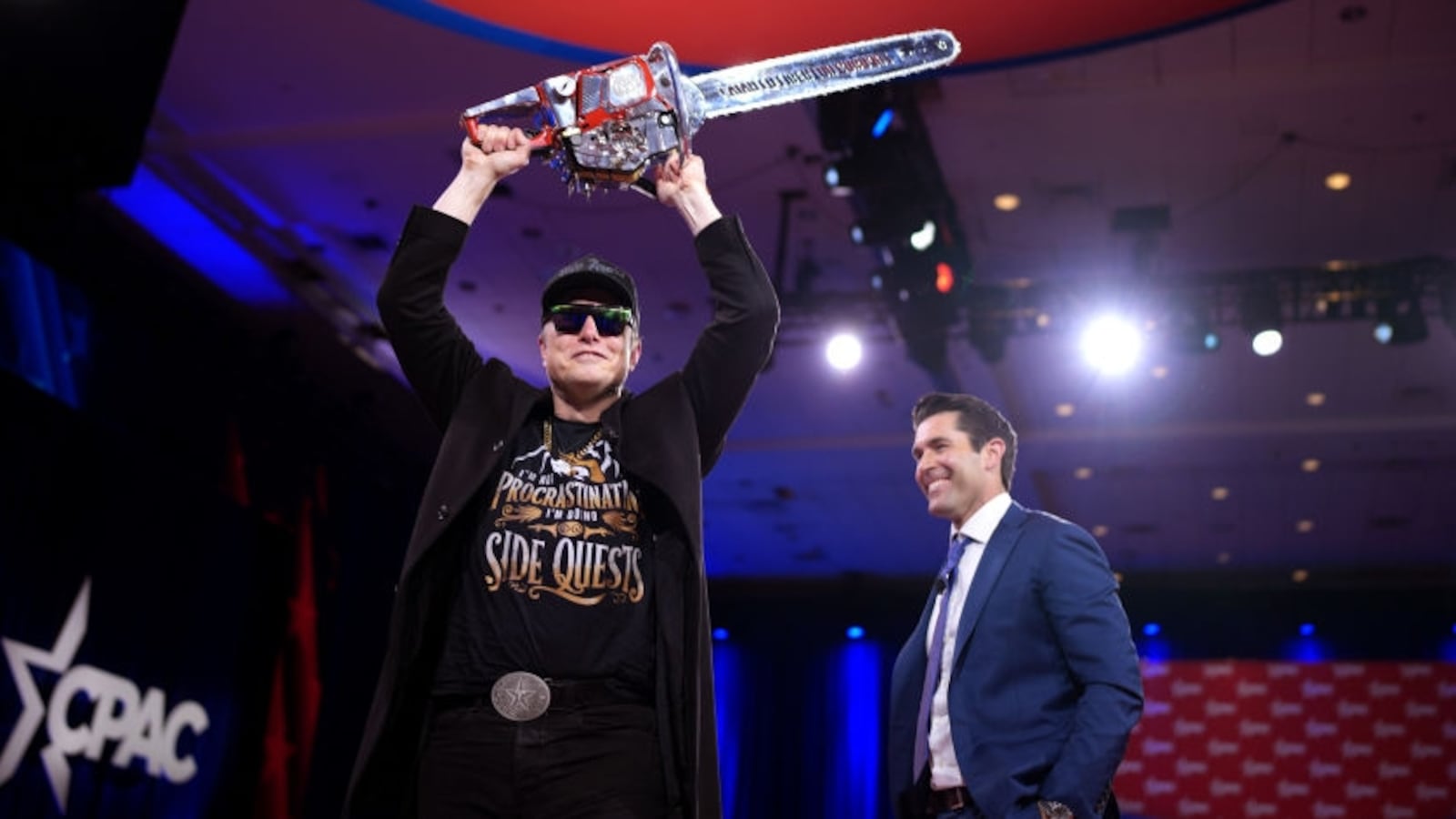 Elon Musk wields a chainsaw as he leaves the stage with Newsmax anchor Rob Schmitt at the Conservative Political Action Conference (CPAC).
