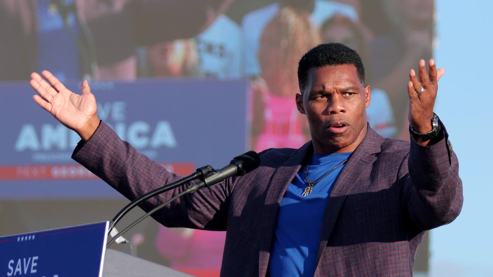 Herschel Walker speaks on stage with his hands raised.