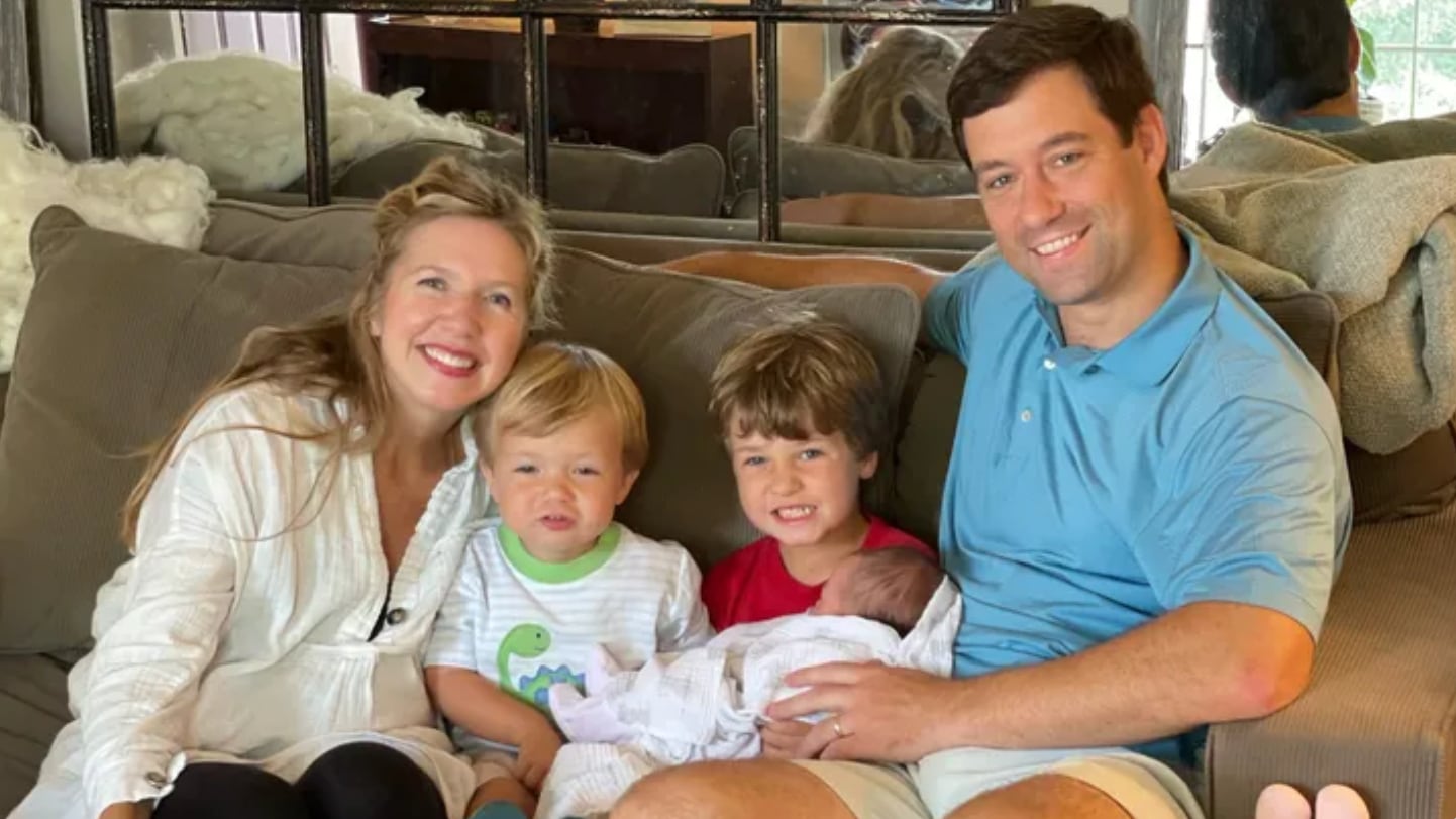 Christopher Wright smiles as he sits on a couch with his wife and three kids.