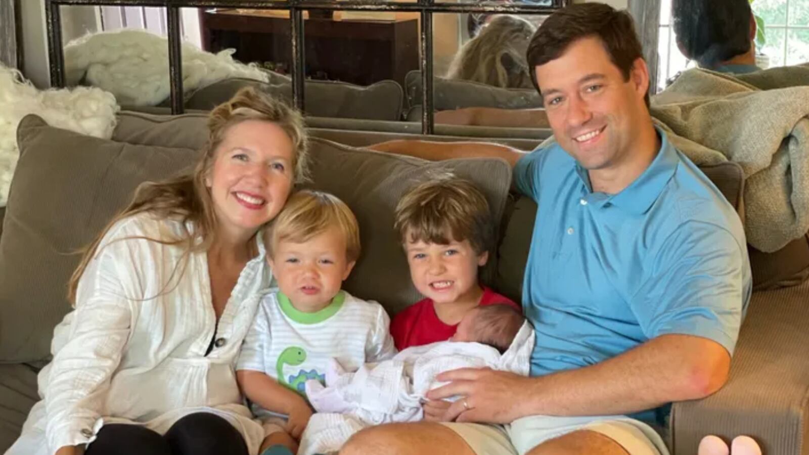 Christopher Wright smiles as he sits on a couch with his wife and three kids.
