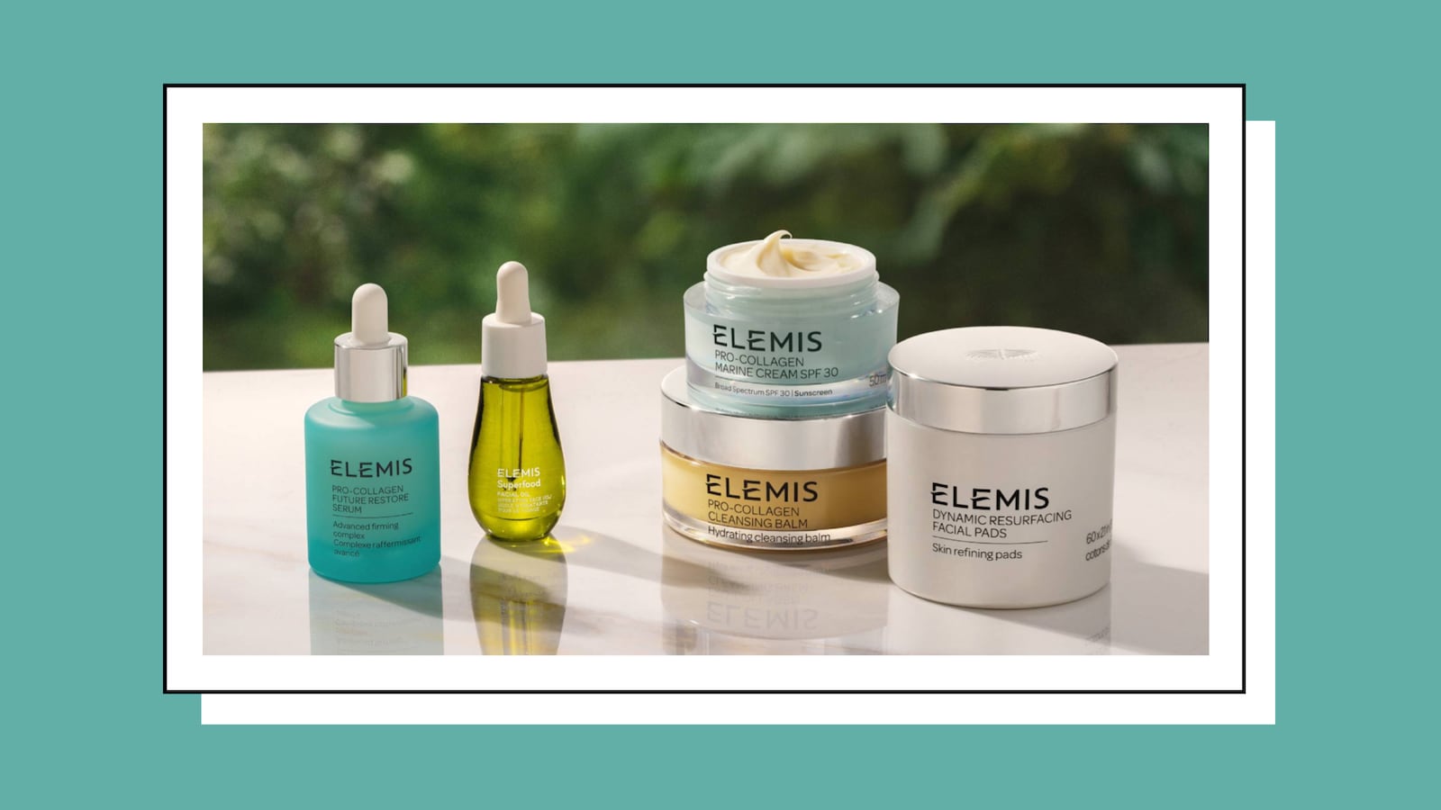 A flatlay of ELEMIS Pro-Collagen skincare products including the Future Restore Serum, Marine Cream SPF 30, and Cleansing Balm arranged on a marble surface with a green outdoor background, set against a teal border.