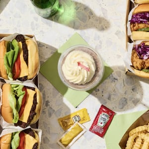 A catered office lunch order from ezCater featuring fried chicken sandwiches, cheeseburgers, crinkle-cut fries, and dipping sauces displayed in an overhead flat-lay.