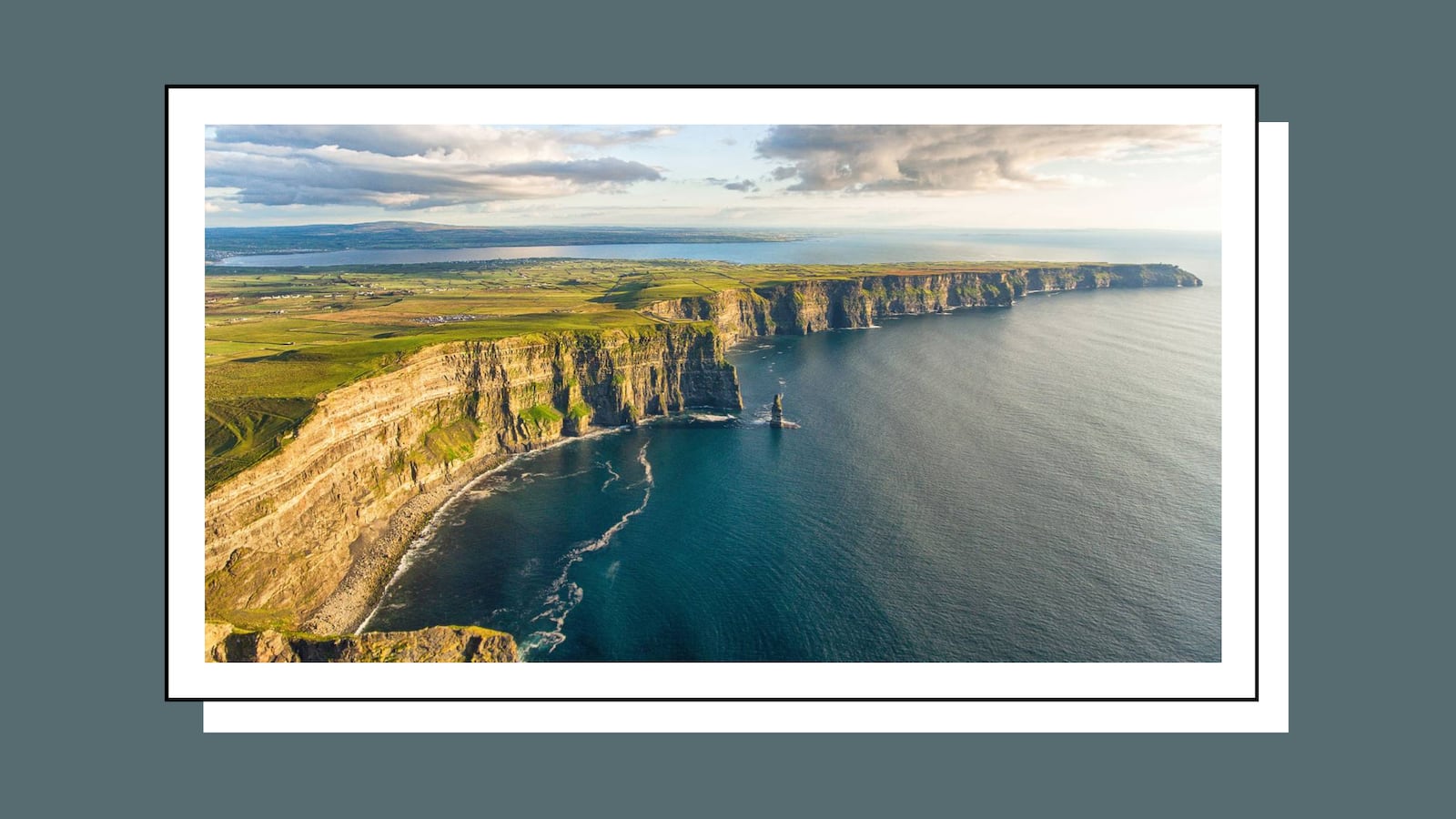 Aerial view of the Cliffs of Moher along the Irish coastline with green fields above and the Atlantic Ocean below