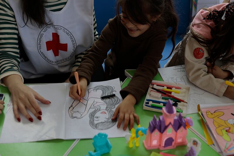 A Red Cross worker and children play with color books.