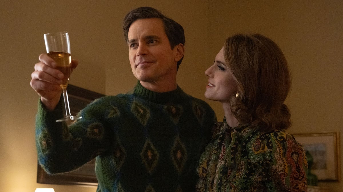 Matt Bomer holds a glass of wine up while Allison Williams holds on to him