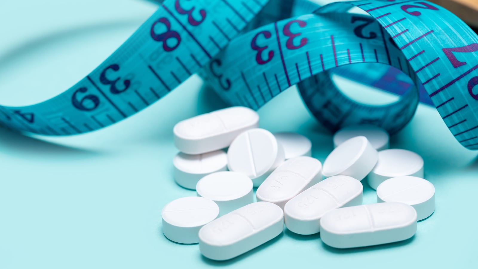 GLP-1 drugs spilling out of pill bottle and measuring tape on blue background