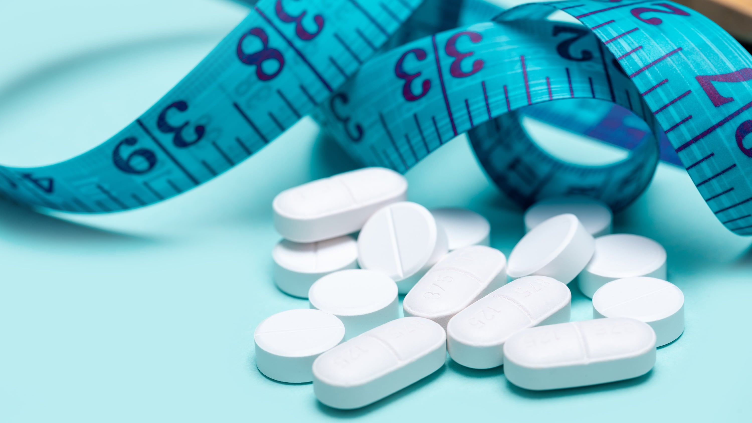 GLP-1 drugs spilling out of pill bottle and measuring tape on blue background