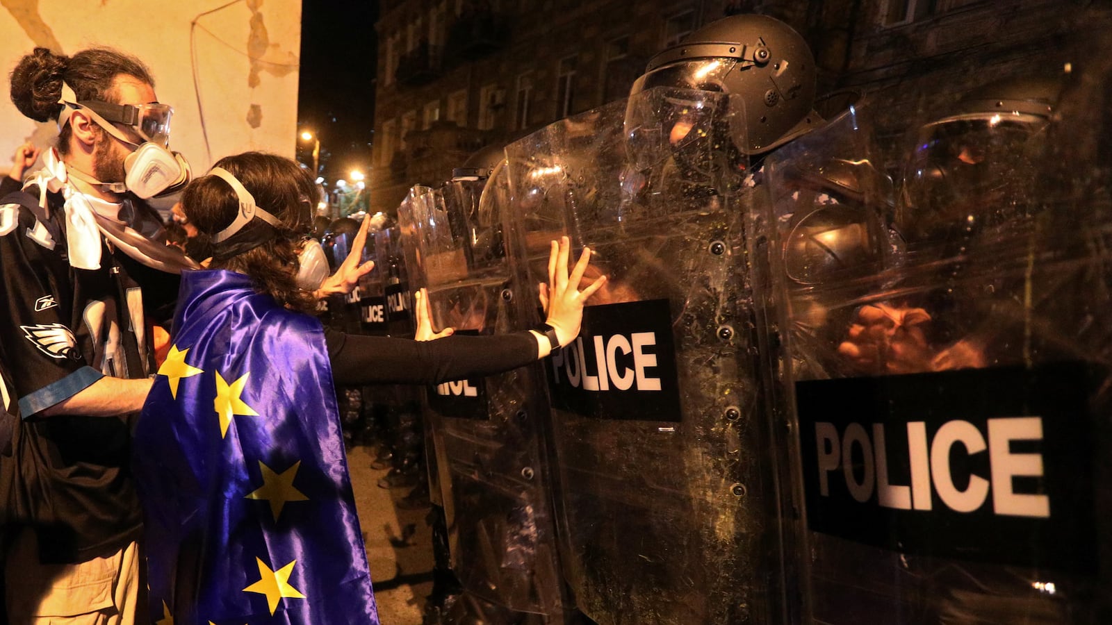 Demonstrators stand in front of police officers with riot gear.