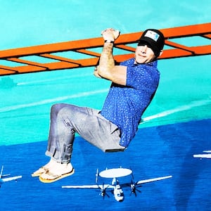 Pete Hegseth hangs on monkey bars with military craft in the background.