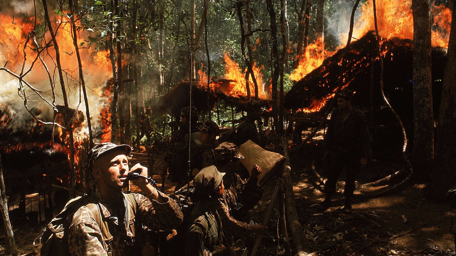 U.S. Army Special Forces Capt. Vernon Gillespie contacting his base camp by radio while Vietnamese soldiers burn down a National Liberation Front hideout.