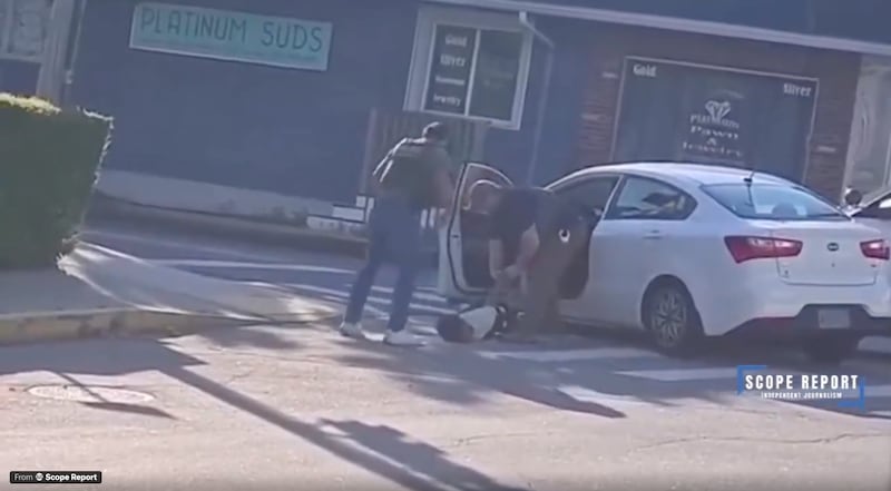Two men in white vests drag a man out of a white Kia Ceed