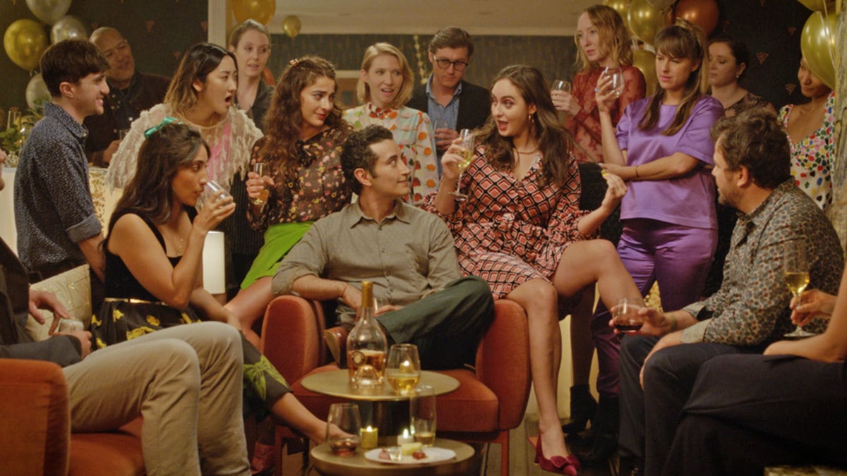 People sit on and around couches in a still from ‘The French Italian’