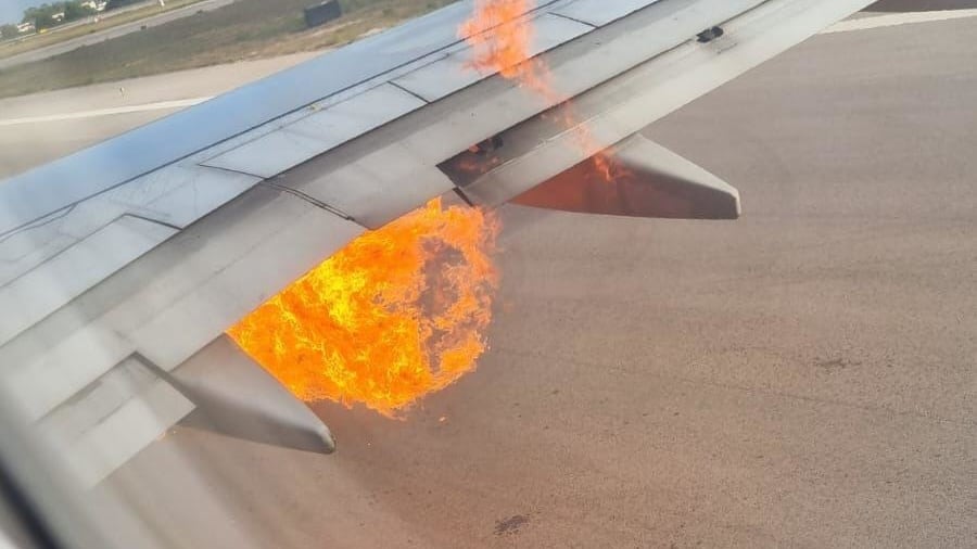 A view from a plane window shows a fireball bursting out from below the jet's wing.