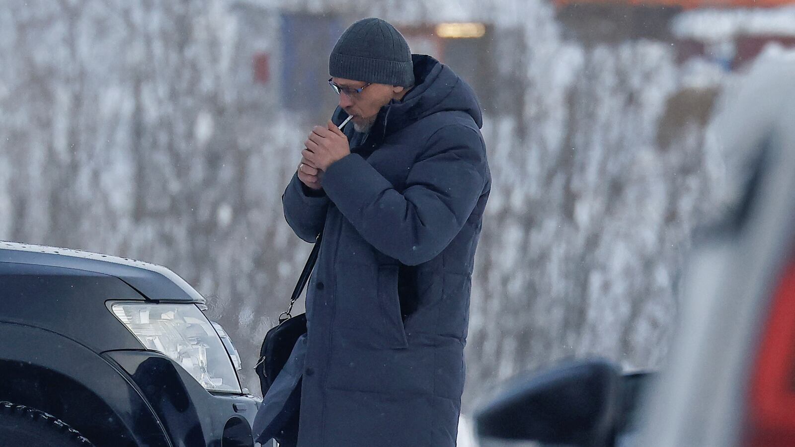 Lawyer Vasily Dubkov lights a cigarette in a snowy parking lot.