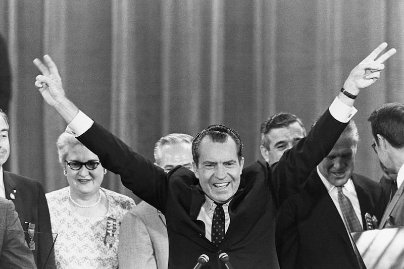 Richard Nixon greets a crowd with his trademark victory symbol. Nixon (1913-1994) was the 37th president of the United States, and was pressured to resign when the details of the Watergate Scandal were revealed.