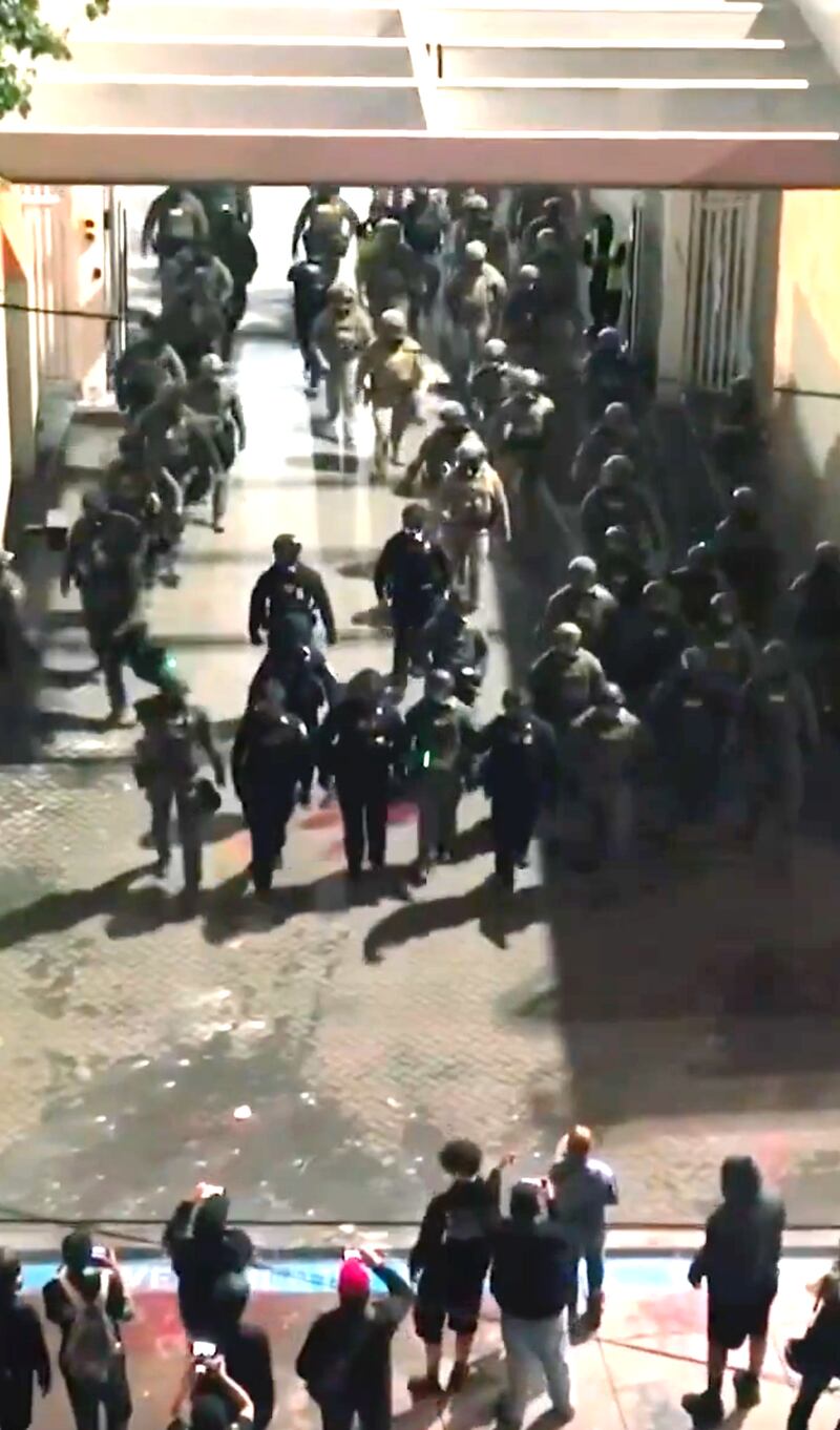 DHS officers march out of the compound towards protestors.