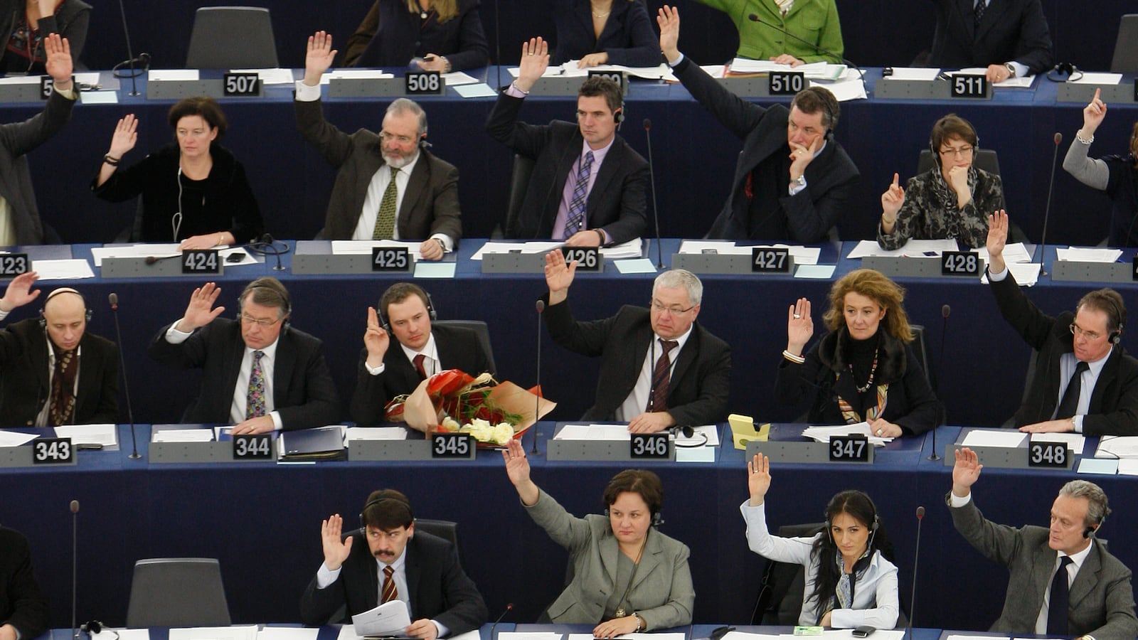 Members of the European Parliament vote with raised hands in seats.
