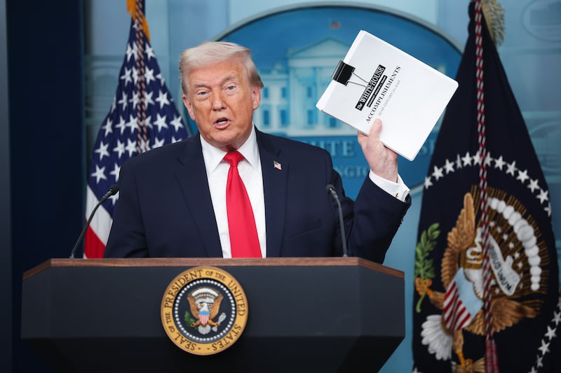 President Donald Trump displays a stack of papers labeled "The White House Accomplishments" as he arrives for a press briefing on January 20, 2026.