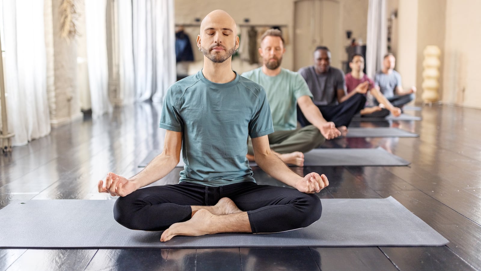 Group of people sitting on mats in lotus padmasana pose. Multiracial group of men meditating in sitting yoga pose in yoga class, mindfulness and meditation.