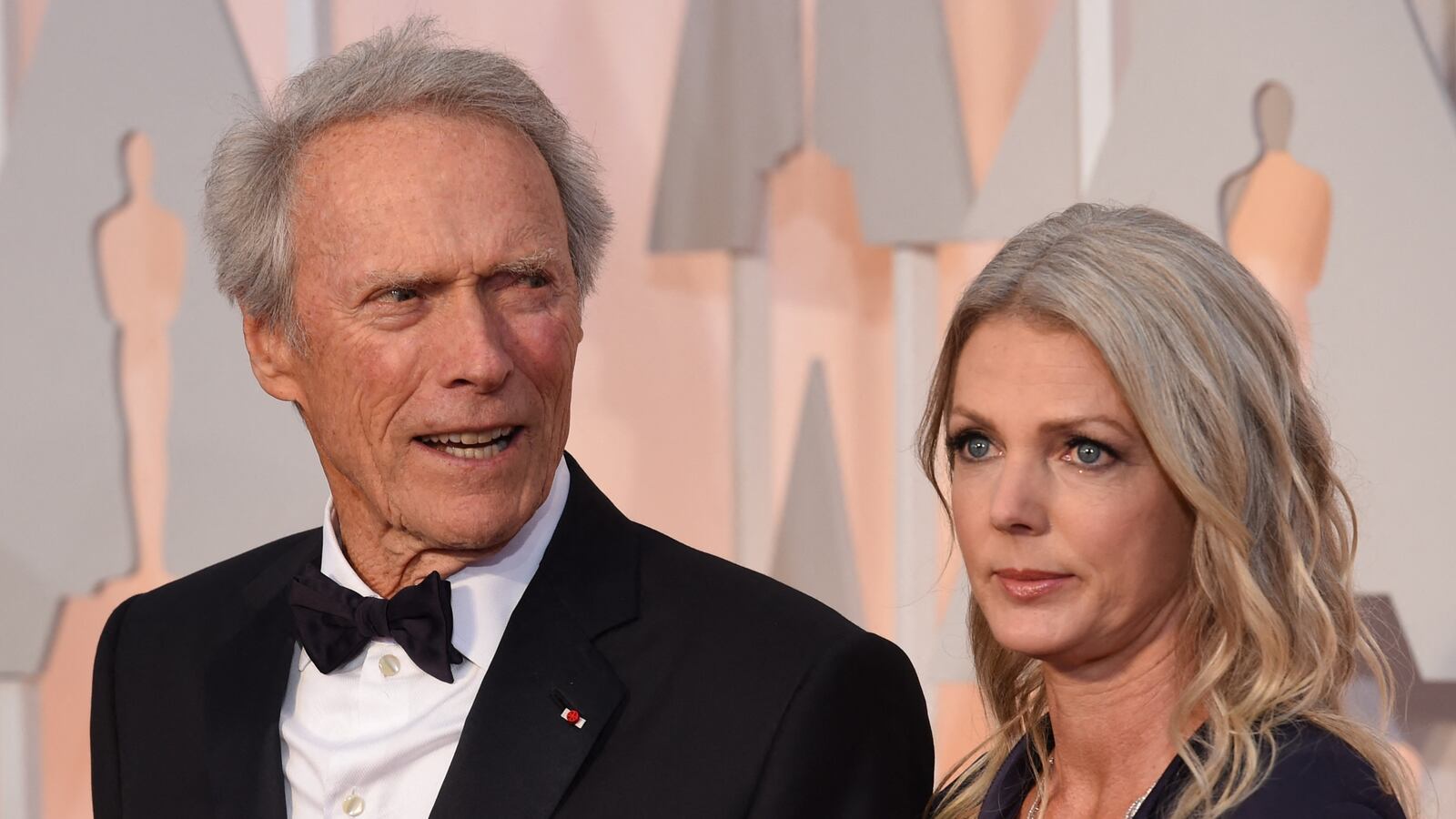 Nominee for Best Picture "American Sniper," Clint Eastwood (L) and Christina Sandera pose on the red carpet for the 87th Oscars on February 22, 2015 in Hollywood, California. AFP PHOTO / MARK RALSTON (Photo by MARK RALSTON / AFP) (Photo by MARK RALSTON/AFP via Getty Images)
