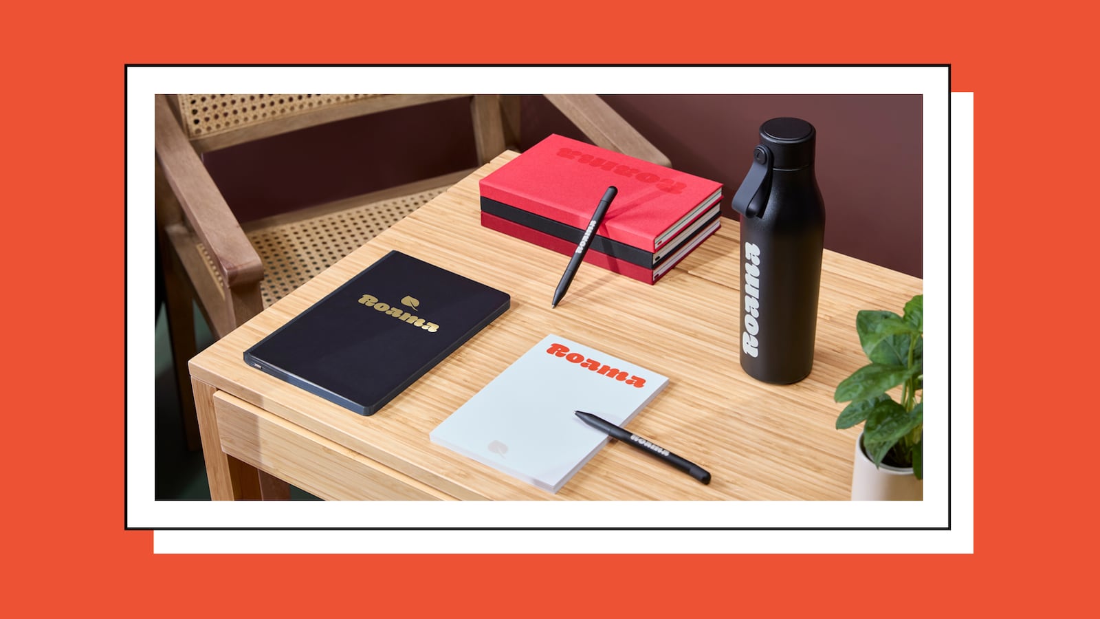 Branded MOO stationery on a wooden desk, including custom notebooks, pens, and a black insulated bottle with logo.