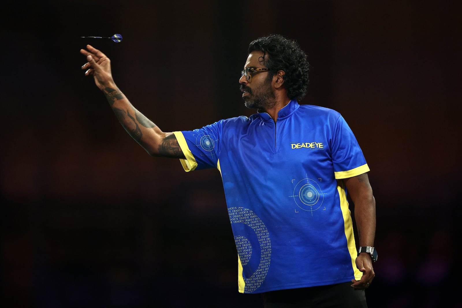 Romesh Ranganathan shows off his tattoo sleeve as he throws a dart during day four of the World Darts Championship in London, England, on December 18, 2024.