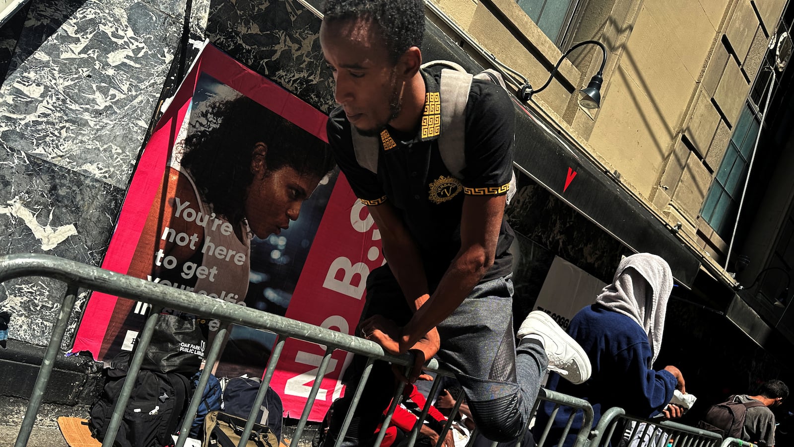 A recently arrived migrant to New York City climbs over a barricade to a line of people waiting on the sidewalk outside the Roosevelt Hotel in midtown, Manhattan.