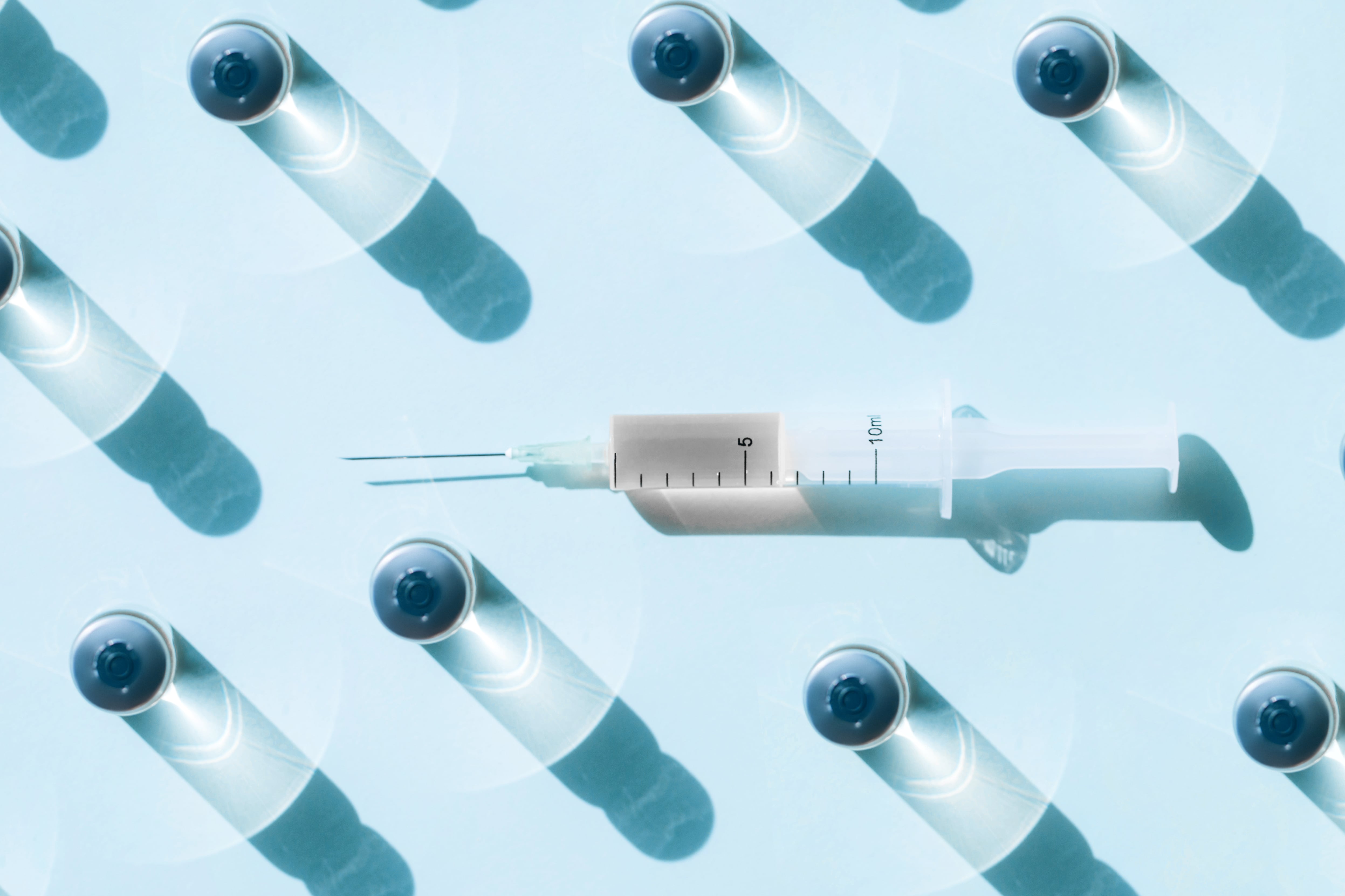 Plastic disposable syringe and glass bottle of drug placed on blue background with shadows and light reflections.
