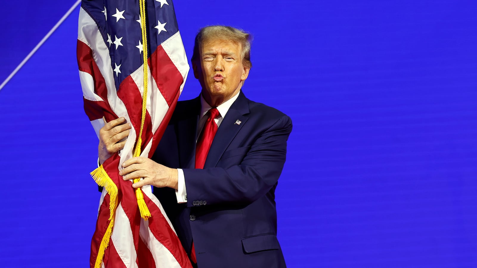Republican presidential candidate and former U.S. President Donald Trump hugs an American flag as he arrives at the Conservative Political Action Conference (CPAC) at the Gaylord National Resort Hotel And Convention Center in National Harbor, Maryland.
