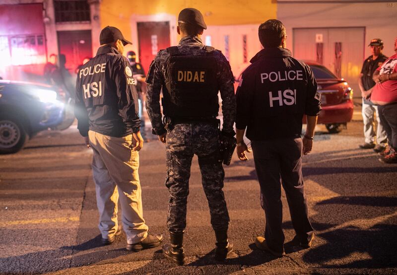 ICE agents with U.S. Homeland Security Investigations (HSI), and a Guatemalan policeman (C) stand at the scene of an early morning raid where a suspected human trafficker (R), was taken into custody