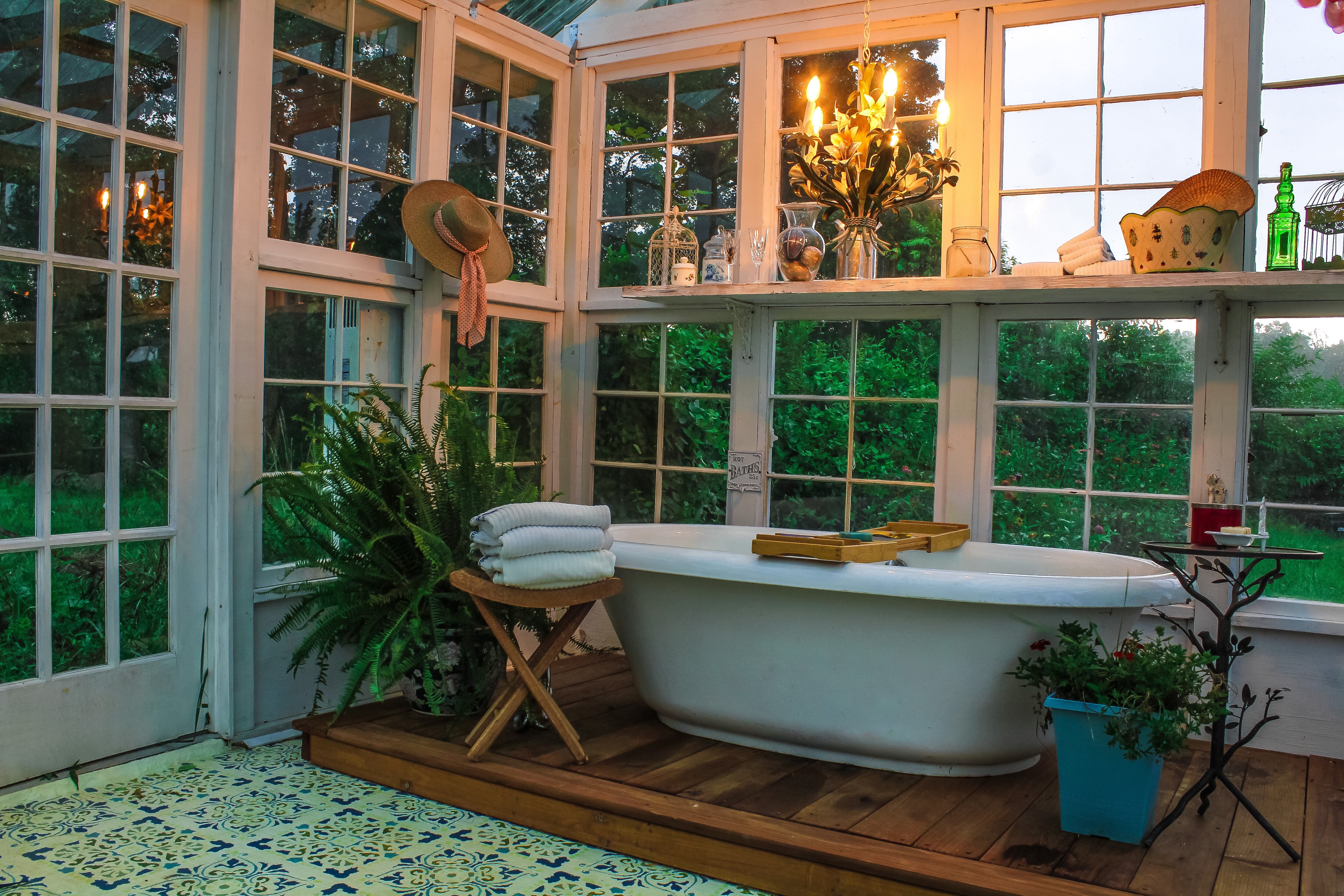 Interior of a greenhouse with a large soaking tub on a wooden platform with a tole chandelier plants towels and a stenciled floor